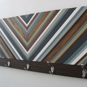 May include: A wooden wall mounted coat rack with a chevron pattern in shades of brown, gray, and white. The rack has five metal hooks.