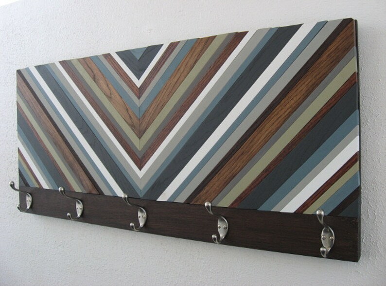 May include: A wooden wall mounted coat rack with a chevron pattern in shades of brown, gray, and white. The rack has five metal hooks.