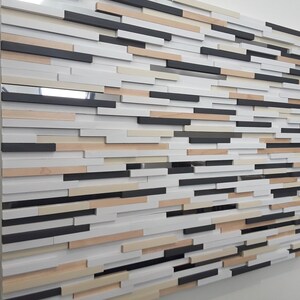 May include: A wall art piece made of wood slats in various shades of brown, white, and black. The slats are arranged in a staggered pattern, creating a textured and modern look.