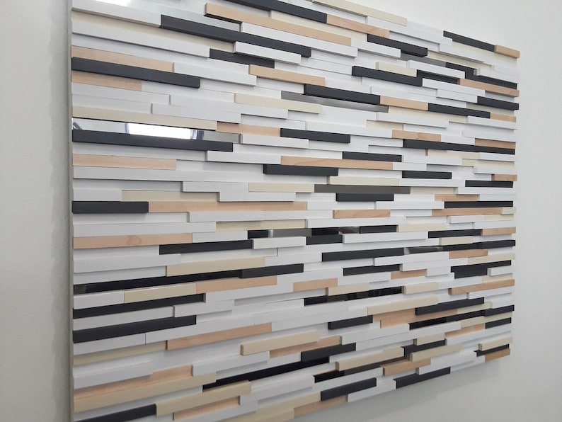 May include: A wall art piece made of wood slats in various shades of brown, white, and black. The slats are arranged in a staggered pattern, creating a textured and modern look.
