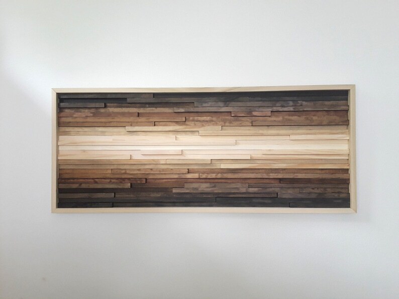 May include: A framed wood wall art piece with a gradient of brown wood tones. The wood is arranged in horizontal rows, creating a layered effect. The frame is a simple, natural wood colour.