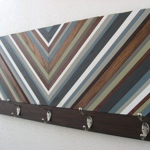 May include: A wooden wall-mounted coat rack with a chevron pattern in shades of brown, gray, and white. The rack has five metal hooks.