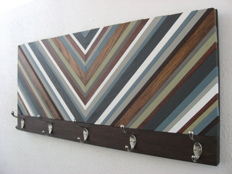 May include: A wooden wall-mounted coat rack with a chevron pattern in shades of brown, gray, and white. The rack has five metal hooks.