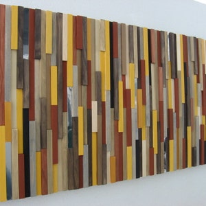 Puede incluir: Una pieza de arte de pared hecha de varias tablas de madera en diferentes colores y anchos. Las tablas est&aacute;n dispuestas en un patr&oacute;n vertical, creando un dise&ntilde;o moderno y abstracto. Los colores incluyen amarillo, marr&oacute;n, rojo y gris.