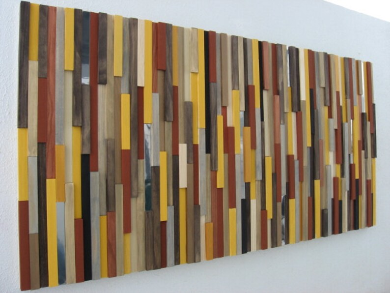 Puede incluir: Una pieza de arte de pared hecha de varias tablas de madera en diferentes colores y anchos. Las tablas est&aacute;n dispuestas en un patr&oacute;n vertical, creando un dise&ntilde;o moderno y abstracto. Los colores incluyen amarillo, marr&oacute;n, rojo y gris.