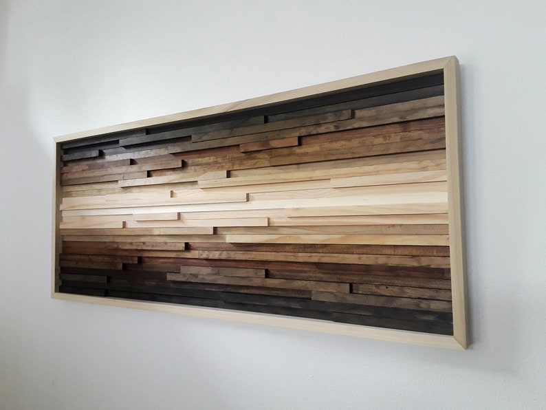 May include: A framed wood wall art piece with a gradient of brown wood tones. The wood is arranged in horizontal strips of varying lengths, creating a layered effect. The frame is a light wood colour.