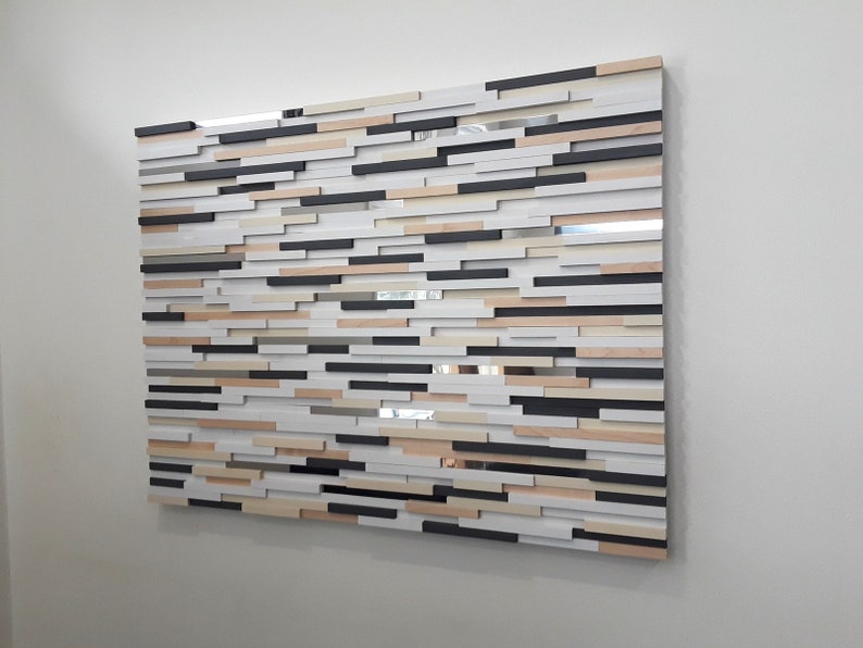 May include: A wall art piece made of various sized rectangular wooden blocks in shades of white, black, brown, and beige. The blocks are arranged in a staggered pattern to create a textured surface.