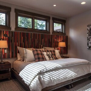 May include: A bedroom with a king-size bed with a white duvet and a headboard made of reclaimed wood. There are two bedside tables with lamps and a painting of trees on the wall.