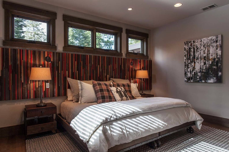 May include: A bedroom with a king-size bed with a white duvet and a headboard made of reclaimed wood. There are two bedside tables with lamps and a painting of trees on the wall.