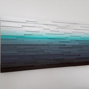 May include: Abstract wall art made of wood painted in shades of white, blue, and gray. The wood pieces are arranged in a horizontal pattern, creating a gradient effect.