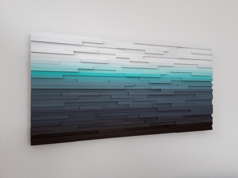 May include: Abstract wall art made of wood painted in shades of white, blue, and gray. The wood pieces are arranged in a horizontal pattern, creating a gradient effect.
