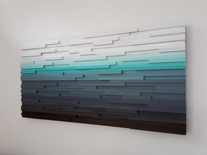 May include: Abstract wall art made of wood with a gradient of colors from white to dark gray, with a turquoise blue band in the middle.