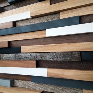 May include: A wall art piece made of various wood planks in different shades of brown, gray, and white. The planks are arranged in a staggered pattern, creating a modern and abstract design.