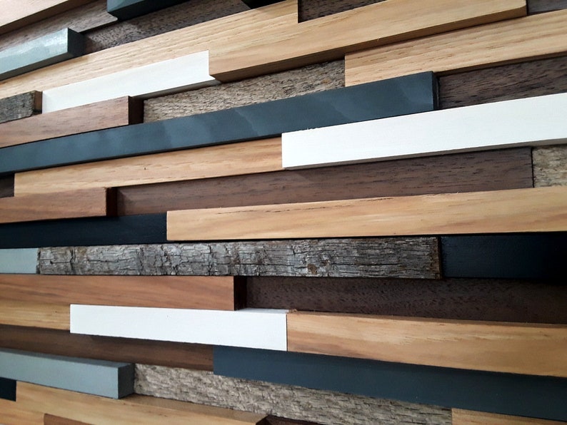 May include: A wall art piece made of various wood planks in different shades of brown, gray, and white. The planks are arranged in a staggered pattern, creating a modern and abstract design.