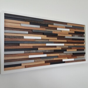 May include: A rectangular wall art piece made of wood with a white frame. The wood is arranged in a horizontal pattern with different shades of brown, gray, and white.