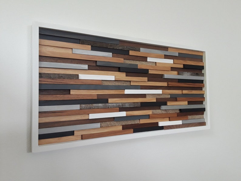 May include: A rectangular wall art piece made of wood with a white frame. The wood is arranged in a horizontal pattern with different shades of brown, gray, and white.