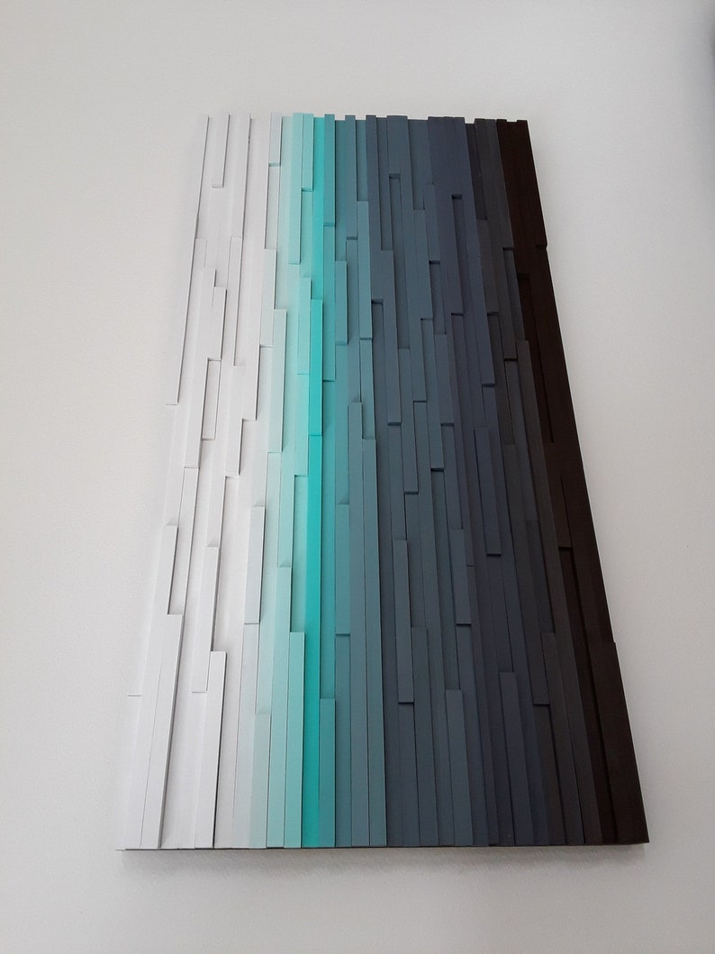 May include: Abstract wall art made of wood painted in shades of white, turquoise, blue, gray, and black. The wood pieces are arranged in vertical rows to create a gradient effect.