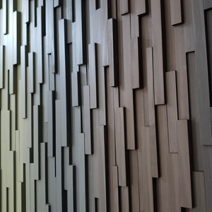 May include: A wall covered in a gradient of wood panels, ranging from light beige to dark brown. The panels are arranged in a staggered pattern, creating a textured and modern look.
