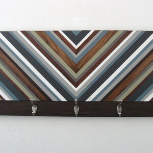 May include: A wooden wall-mounted coat rack with a chevron pattern in shades of brown, gray, and white. The rack has five metal hooks.