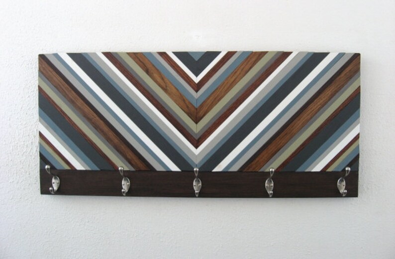 May include: A wooden wall-mounted coat rack with a chevron pattern in shades of brown, gray, and white. The rack has five metal hooks.