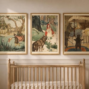 Puede incluir: Un conjunto de tres láminas de arte enmarcadas con ilustraciones de cuentos de hadas de estilo vintage. La lámina izquierda muestra un gato con capa, la central una figura con capucha roja y un lobo, y la derecha muestra osos en un dormitorio.
