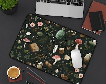 May include: A dark green mousepad with a whimsical pattern of mushrooms, crystals, flowers, and potion bottles. The design includes a book, acorns, and various botanical elements. A white mouse sits on the pad, next to a laptop.