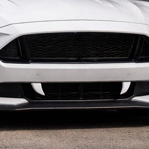 May include: A white sports car with a black grille and distinctive front end design. The car features sleek headlights and a low profile, emphasizing its sporty aesthetic. The front bumper has unique, stylized accents.