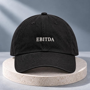 May include: A black baseball cap featuring the word EBITDA embroidered in white capital letters on the front panel. The cap has a structured crown, a curved brim, and stitched eyelets for ventilation, presenting a clean and simple design.