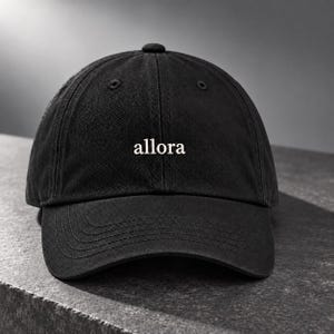 Op de afbeelding: Een zwarte baseballpet met een gestructureerde kroon en een gebogen klep. Het woord "allora" is in witte, kleine schreefletters op het midden van de voorkant geborduurd. De pet heeft zes panelen met bijpassende stiksels en een knoop.