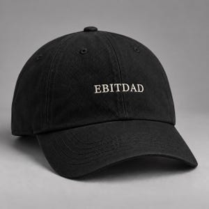 May include: A black baseball cap featuring the text "EBITDAD" embroidered in white thread across the front panel. The cap has a structured crown, a curved brim with visible stitching, and eyelets for ventilation on the top panels.