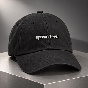 May include: A black baseball cap with a six-panel construction and a curved brim. The word spreadsheets is embroidered in white, lowercase, serif font across the front center of the cap. The fabric has a slightly faded, matte texture.