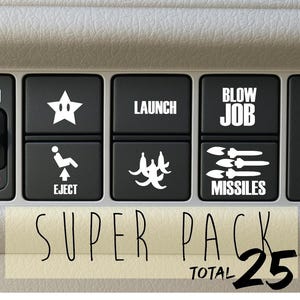 Könnte beinhalten: Nahaufnahme von schwarzen Knöpfen mit weißen Grafiken und Text. Die Knöpfe zeigen einen Stern, eine auswerfende Person, das Wort "LAUNCH", Bananen, die Wörter "BLOW JOB" und Raketen. Der Text "SUPER PACK" und "TOTAL 25" ist ebenfalls sichtbar.