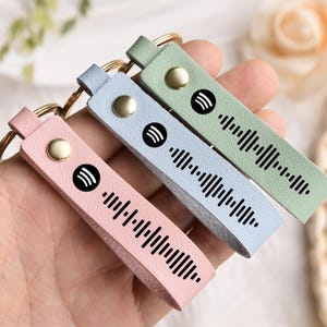 May include: Three keychains with different coloured leather straps and a black Spotify logo and barcode. The keychains are pink, light blue and green.