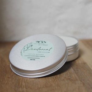 Peut inclure: Une boîte en étain argentée avec une étiquette blanche qui indique "Déodorant - Lisse citronnée - Parfum Agrumes - Cultivé & transformé en Ardèche - 100 ML".