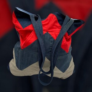 Könnte beinhalten: Eine blaue und rote Patchwork-Tragetasche mit langen Riemen. Die Tasche ist aus Jeansstoff und hat ein Chevron-Muster.