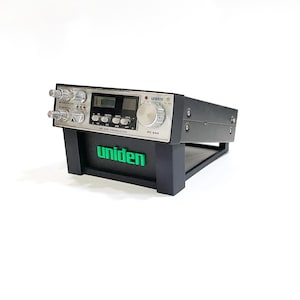 May include: A black and silver Uniden CB radio transceiver, model PC 66, featuring various knobs, buttons, and a digital display. The radio is mounted on a black stand with the green Uniden logo. Designed for communication.