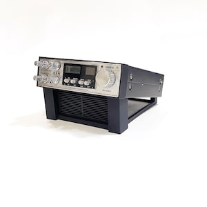 May include: A Uniden PC 664 CB radio transceiver. The device has a silver face with knobs, buttons, and digital displays. The body is black and mounted on a black stand. The model name and other text are visible on the face.