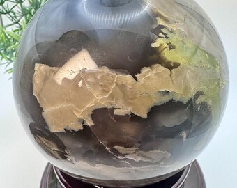 May include: A large, clear agate sphere with brown, white, and green inclusions. The sphere is sitting on a dark wooden stand.