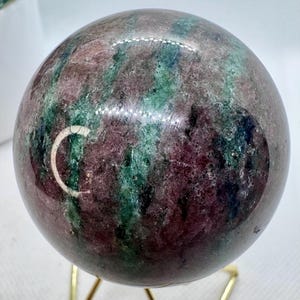 May include: A polished green and pink sphere of ruby zoisite, also known as anyolite, on a gold metal stand.