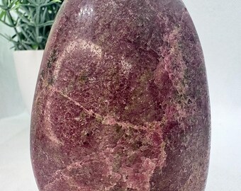 May include: A large, freeform, pink and green polished gemstone with a rough, natural texture. The stone has a variety of shades of pink and green, and it is very sparkly.