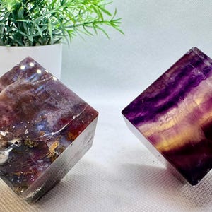 May include: Two polished fluorite cubes, one with purple and yellow hues, the other with red, purple, and white hues.