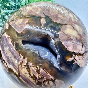 May include: A large, polished, multi-colored sphere of agate with a natural crack running through the center. The sphere is sitting on a gold metal stand with three legs.