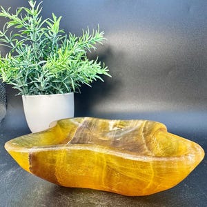 May include: A large, yellow, irregularly shaped bowl made of polished stone. The bowl has a smooth, glossy finish and is perfect for serving snacks or decorative items.