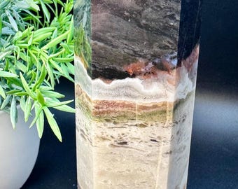 May include: A multi-colored, layered, pointed crystal with a black top. The crystal has a variety of colors including brown, white, and green.