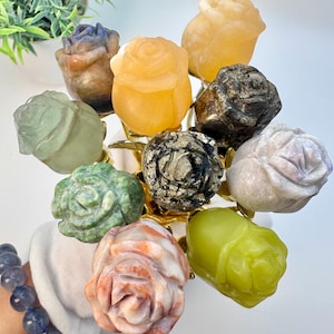 May include: A bouquet of ten rose-shaped crystal carvings in various colors, including green, orange, white, and gray. The roses are arranged on a gold-colored stand.
