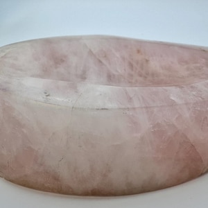 Puede incluir: Un cuenco grande de forma ovalada tallado en una sola pieza de cuarzo rosa. El cuenco tiene una superficie lisa y pulida y un color rosa claro.