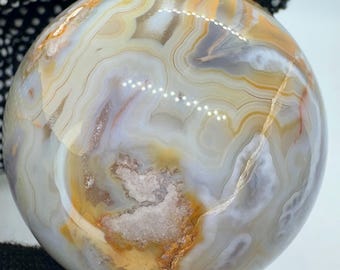 May include: A polished agate sphere with swirling patterns of white, brown, and orange. The sphere is smooth and has a high gloss finish.