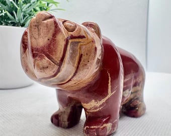 May include: A hand-carved stone bear sculpture with red and white marbling. The bear is standing on all fours with its head tilted up.