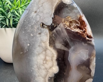 May include: A large, freeform, polished agate with a grey, white, and brown color pattern. The agate has a smooth, polished surface and is a natural stone.