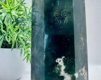 May include: A green and white agate crystal point, also known as a green moss agate, with a pointed top and a hexagonal base.